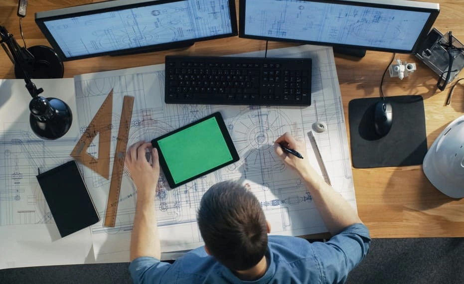 Civil engineer using paper documents from engineering plotters and digital plans to work on a project